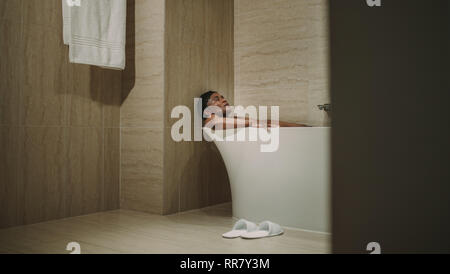 Weibliche entspannen in der Badewanne mit geschlossenen Augen. Reifen afrikanische Frau in der Badewanne liegen. Stockfoto