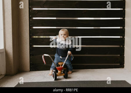 Kostbare adorable kleine süße blonde Baby Kleinkind Junge Spielen draussen auf Holzspielzeug Fahrrad Roller Mobile lächelt in die Kamera und Spaß Stockfoto