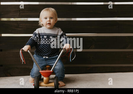 Kostbare adorable kleine süße blonde Baby Kleinkind Junge Spielen draussen auf Holzspielzeug Fahrrad Roller Mobile lächelt in die Kamera und Spaß Stockfoto