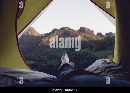 Entspannen Frau liegend und Bein auf der Decke im Zelt kreuz und Blick auf die Berge im Sonnenuntergang auf Camping Urlaub Ferien Stockfoto