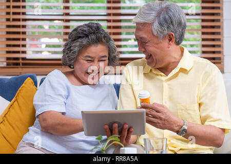 Asiatische senior Paar verwenden tablet Video Konferenz mit Arzt über Pille beim Sitzen auf dem Sofa zu Hause, Senior lernen Technologie zu verwenden. Das Altern zu Hause Stockfoto