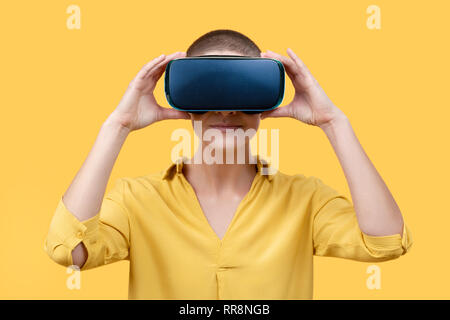 Junge Frau in ihrem 30s mit Virtual reality Brillen. Frau mit VR-Brille isoliert auf gelben Hintergrund. VR-erfahrung Konzept. Stockfoto