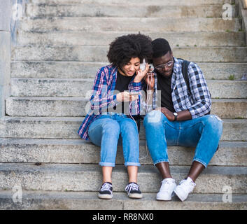 Hipster casual Paar schwarze afrikanische Frau und Mann verwenden technologyh Smartphone Musik zusammen mit der gleichen Kopfhörer-Jugendliche und die Beziehungen zu hören Stockfoto