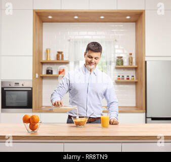Junge Mann in einem Hemd gießen Milch in eine Schüssel Müsli zum Frühstück in einer modernen Küche Stockfoto