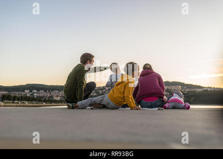 Familie von fünf sitzen auf hölzernen Pier mit dem Vater und zeigte auf etwas in der Ferne. Stockfoto