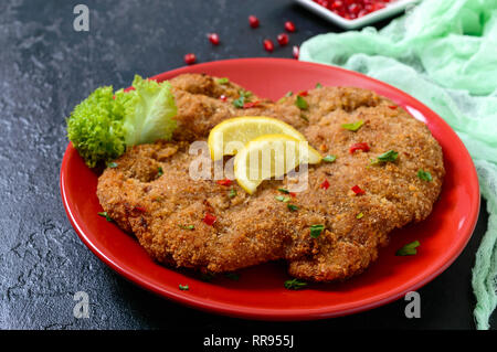 Große Wiener Schnitzel auf einer roten Platte mit Zitrone auf einem schwarzen Hintergrund. Fleischgericht. Stockfoto