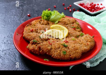 Große Wiener Schnitzel auf einer roten Platte mit Zitrone auf einem schwarzen Hintergrund. Fleischgericht. Stockfoto