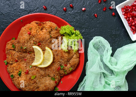 Große Wiener Schnitzel auf einer roten Platte mit Zitrone auf einem schwarzen Hintergrund. Fleischgericht. Ansicht von oben, flach. Stockfoto