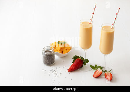 2 Gläser frische Mango Smoothie oder Mango Milchshake, mit Chia Samen in den jar, Mangostückchen in Porzellan Schüssel und nur wenige echte frische Erdbeeren. Kostenlos Stockfoto