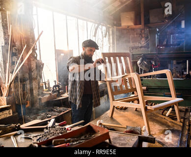Ein Handwerker in seiner Werkstatt arbeitet auf einem Sessel Gestell Stockfoto