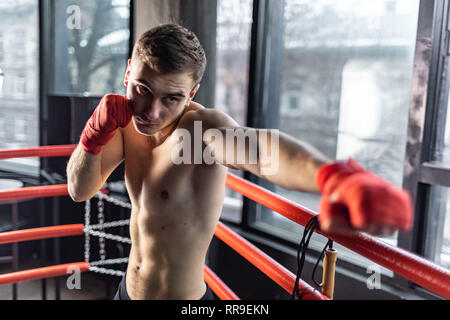 Punhing Mann mit roten Bandagen im Ring vor der breiten Fenster Stockfoto