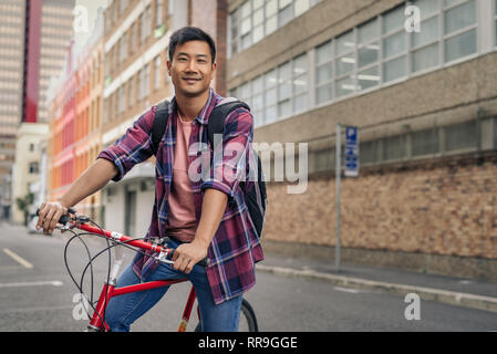 Lächelnden jungen Mann, der mit seinem Fahrrad in der Stadt Stockfoto