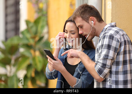 Paar hören online Musik von smart phone Suche Lieder auf der Straße Stockfoto