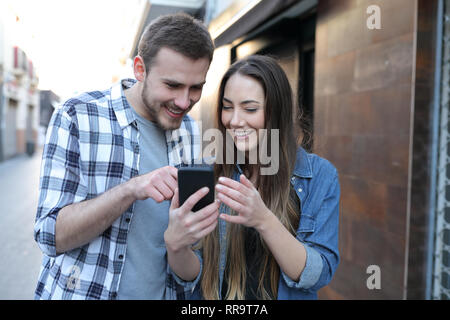 Zwei glückliche Freunde oder Paare mit einem Smart Phone zu Fuß auf der Straße Stockfoto