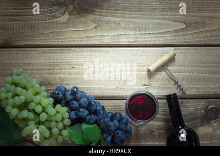 Geöffnete Flasche Rotwein mit einem Glas, Korkenzieher und reife Trauben auf einem hölzernen Hintergrund. Kopieren Sie Raum und Ansicht von oben. Stockfoto