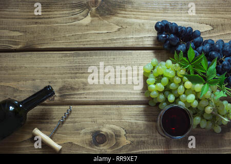 Geöffnete Flasche Rotwein mit einem Glas, Korkenzieher und reife Trauben auf einem hölzernen Hintergrund. Kopieren Sie Raum und Ansicht von oben. Stockfoto