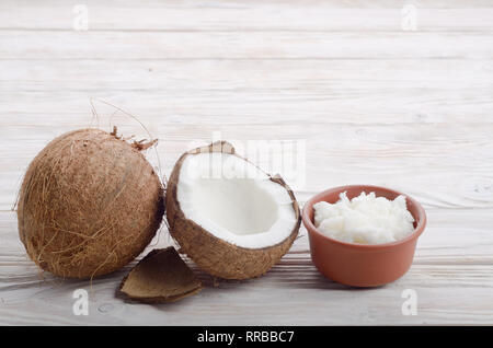 Hintergrund der Kokosnuss, Kokosnussschalen, Schwer öl in Ton Schüssel auf weiße Holztisch Stockfoto
