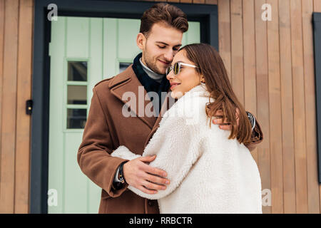 Liebevolle Frau tragen beige Mantel und Gläser ihre Geliebte umarmen Stockfoto