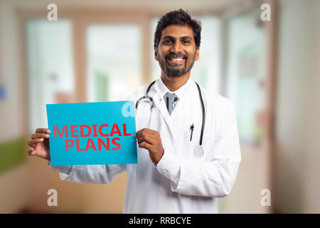 Lächelnd indischen Arzt Mann hält in der Hand blaues Papier mit medizinische Pläne roten Text als Konzept Stockfoto