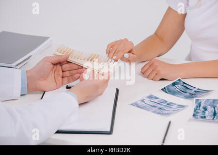 7/8-Ansicht von Frau zeigt mit dem Finger auf die Zähne Farbpalette während der Konsultation mit Zahnarzt isoliert auf weißem Stockfoto
