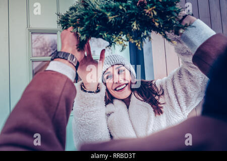Frau tragen warme Mütze zu Weihnachten Kranz für die Dekoration von Haus Stockfoto