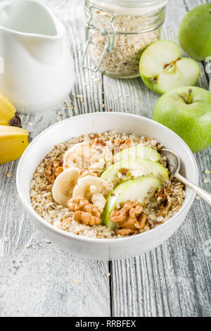 Gesundes Frühstück Müsli mit Nüssen ad Früchte - Apfel, Banane, Walnüsse, mit Milch auf hölzernen Background Copy space Stockfoto