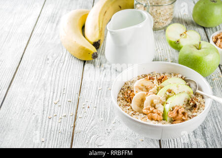 Gesundes Frühstück Müsli mit Nüssen ad Früchte - Apfel, Banane, Walnüsse, mit Milch auf hölzernen Background Copy space Stockfoto