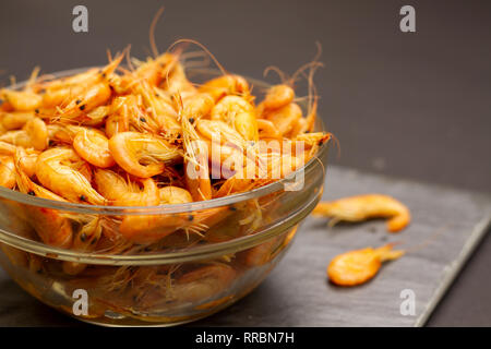 Eine Glasschale mit köstlichen Orangen Garnelen auf einem grauen Tabelle. In der Nähe im Hintergrund sind zwei Gekochte Garnelen. Eine Platte der Garnelen. Snacks und Vorspeise Stockfoto