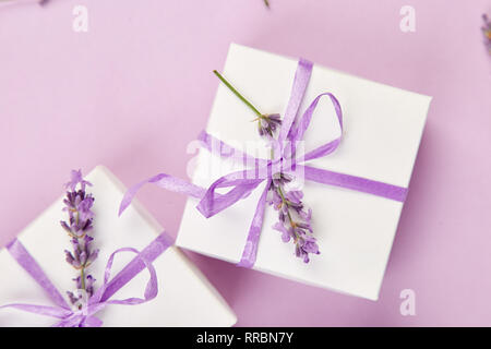 Weiß Geschenkbox mit violetten Band und Blumenstrauß Blume Lavendel auf rosa Hintergrund. Feier, Geburtstag. Dekoration präsentieren. Flach. Kopieren Sie Platz. Stockfoto