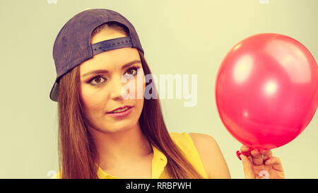 Junges Mädchen, lustig dumme Gesichter. Junge trendige Frau in Jeans cap halten roten Ballon. Stockfoto