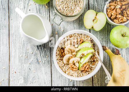 Gesundes Frühstück Müsli mit Nüssen ad Früchte - Apfel, Banane, Walnüsse, mit Milch auf hölzernen Background Copy space Stockfoto