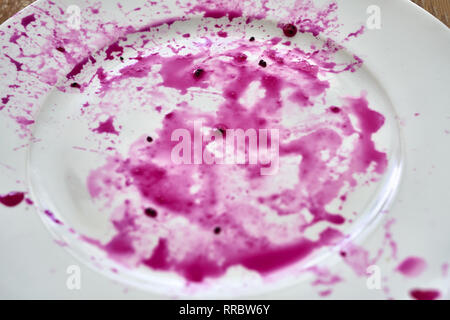 Rosa Flecken der Saft von roter Drache Obst auf dem weißen Teller auf der Holzoberfläche. Es gibt mehrere dunkle Samen auf Ihnen. Closeup top Foto anzeigen. Horizo Stockfoto