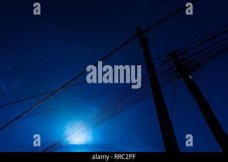 Stöcke mit Elektrizität und Telekommunikation Kabel von unten gegen den blauen Himmel Hintergrund gesehen. Stockfoto