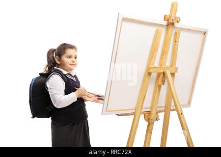 Kleines schulmädchen Holding eine Farbpalette und einer Bürste und stand vor einer Leinwand auf weißem Hintergrund Stockfoto