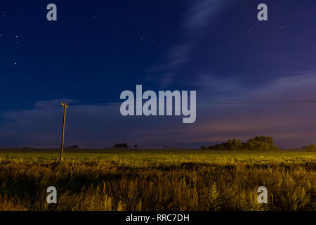 Feld gesät in den Außenbezirken der Stadt. Nacht Blick auf eine Landschaft. Wolken laufen durch den Wind. Geringe Spuren von Sternen. Beleuchtung Post mit einem sm Stockfoto