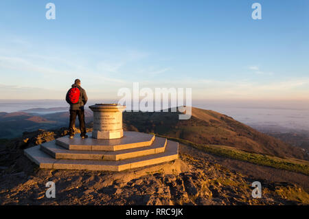 Ein einsamer Wanderer auf dem Gipfel des Worcestershire Beacon, Malvern Hills, Worcestershire, an einem nebligen Winter sunsrise. UK. Stockfoto