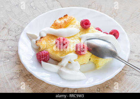 Quark Auflauf mit Himbeeren, Honig, saure Sahne und metallischen Löffel auf weiße Platte auf Holz geschnitten. Stockfoto
