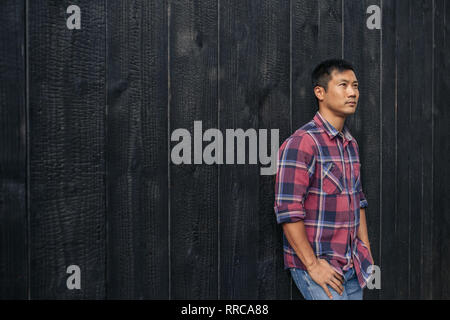 Selbstbewussten jungen asiatischen Menschen gegen eine dunkle Wand außerhalb Schiefen Stockfoto