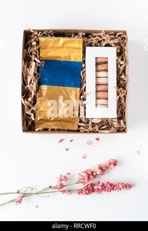 Französische Makronen mit pack Kaffee in braun Handwerk Papier Geschenkbox. Süße macarons in Geschenkverpackung und getrocknete Blumen auf weißem Tabelle. Ansicht von oben, flach. Stockfoto