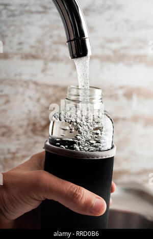 Nahaufnahme von einem jungen Mann cacausian füllen Sie ein Glas wiederverwendbare Trinkflasche mit Wasser aus einem Hahn ein gefiltertes Wasser Station oder eine häusliche Küche Stockfoto