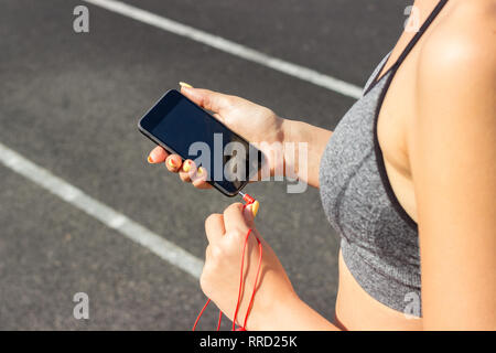 Runner girl Holding Smartphone und fügt Kopfhörer mit dem Telefon. Training am Morgen Zeit. Menschen Sport und Fitness Concept. Stockfoto