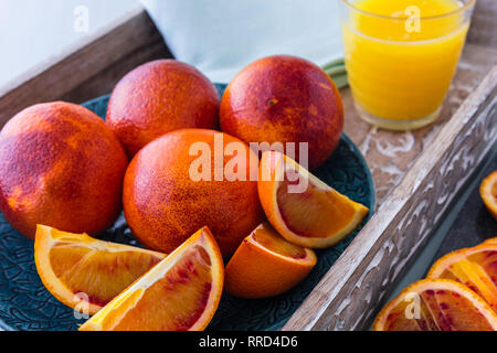 Blutorangen Ganze und Aufgeschnittene auf Platte und Fach mit einem Glas Orangensaft im Hintergrund Stockfoto