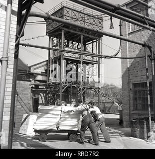 1950er Jahre, zwei männliche Arbeitnehmer, einen Trolley von fertigen Papier außerhalb einer Drucken arbeitet am Brittains Papierfabrik, England, UK. Stockfoto