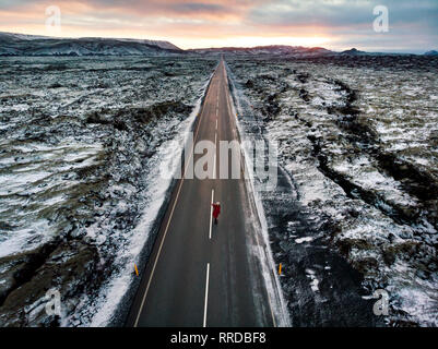 Weibliche Reisende auf isländischen Straße durch Lavaebenen bedeckt mit Schnee umgeben Stockfoto