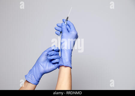 Closeup Arzt oder Krankenschwester Hände in Latex medizinische lila Handschuhe Holding eine transparente Spritze mit scharfen Nadel. Сoncept Ablehnung von Impfungen Stockfoto