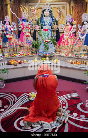 Ein anonymer Hinduistische Frau kniet im Gebet und Meditation vor Statuen von Gottheiten in Queens, New York City Stockfoto