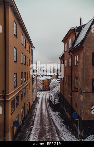 Schmale leere Straße mit alten Gebäuden an einem verschneiten Wintertag mit dem Fluss im Hintergrund, Stockholm, Schweden Stockfoto