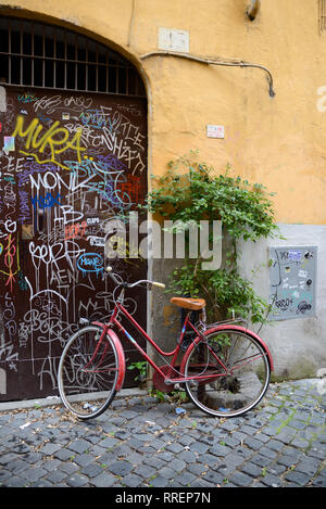 Street Scene mit Abgestellten roten Fahrrad und Graffiti bedeckt ockerfarbenen Wände im eleganten und historischen Viertel Trastevere, Rom, Italien Stockfoto