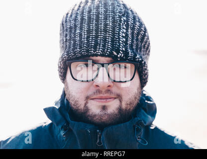 Ein männliches Portrait von einem schönen und robusten jungen Mann mit Brille und einem Wooly hat in einer kalten Umgebung mit warmer Kleidung Stockfoto