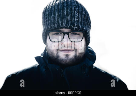 Ein männliches Portrait von einem schönen und robusten jungen Mann mit Brille und einem Wooly hat in einer kalten Umgebung mit warmer Kleidung Stockfoto